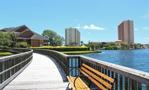 A wooden boardwalk with benches, a water body, and buildings in the background. - South Hampton 301 (Myrtle Beach)
