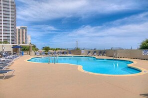 A swimming pool with lounge chairs and a high-rise building in the background. - South Hampton 301 (Myrtle Beach)
