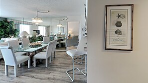 Un espace de restauration moderne avec des tables en verre et des chaises blanches, un lustre et une œuvre d’art encadrée accrochée au mur.