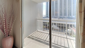 Ein Balkon mit Blick auf hohe Gebäude, einem weißen Geländer und einer Vase mit Trockenpflanzen.