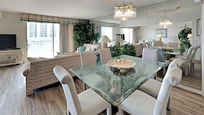 Uma sala de estar ampla com uma mesa de jantar de vidro, mobiliário moderno e uma grande janela com vista para a cidade.