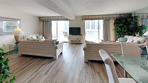 Uma sala de estar ampla, com um conjunto de sofás, uma televisão e uma mesa de centro de vidro.