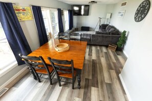 A dining area with a wooden table and chairs, a sofa, a television, and a clock on the wall.