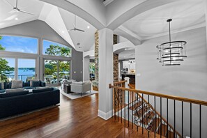 A spacious living area with a large window overlooking a scenic view, a modern staircase, and a kitchen area. - Sunset on Ballycastle (Mooresville)