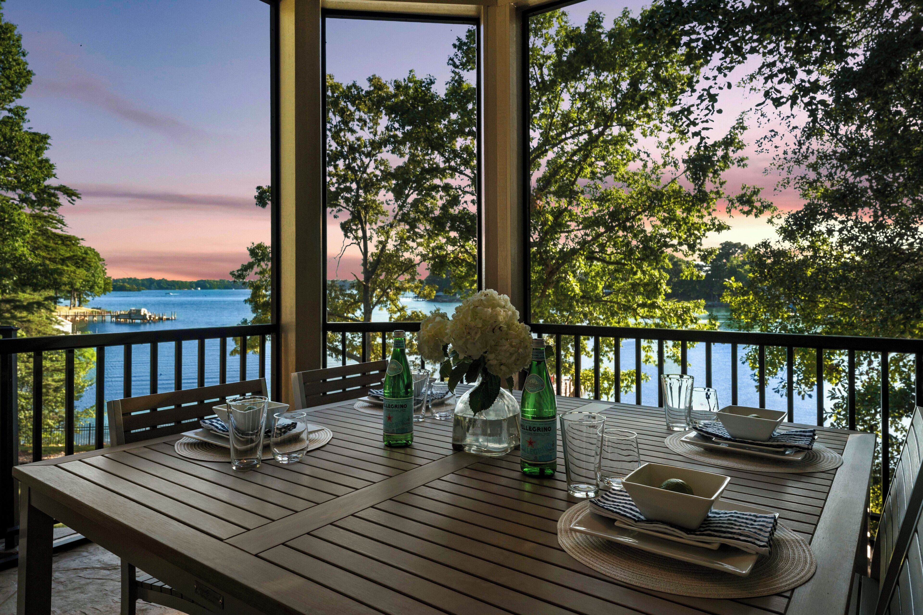 Mesa de madera lista para cenar con vista a un lago y al atardecer.