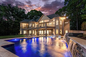 Ein zweistöckiges Haus mit Swimmingpool, Sitzgelegenheiten im Freien und einem Wasserfall.