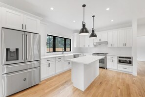 Una cocina moderna con armarios blancos, electrodomésticos de acero inoxidable, una isla grande e iluminación colgante.