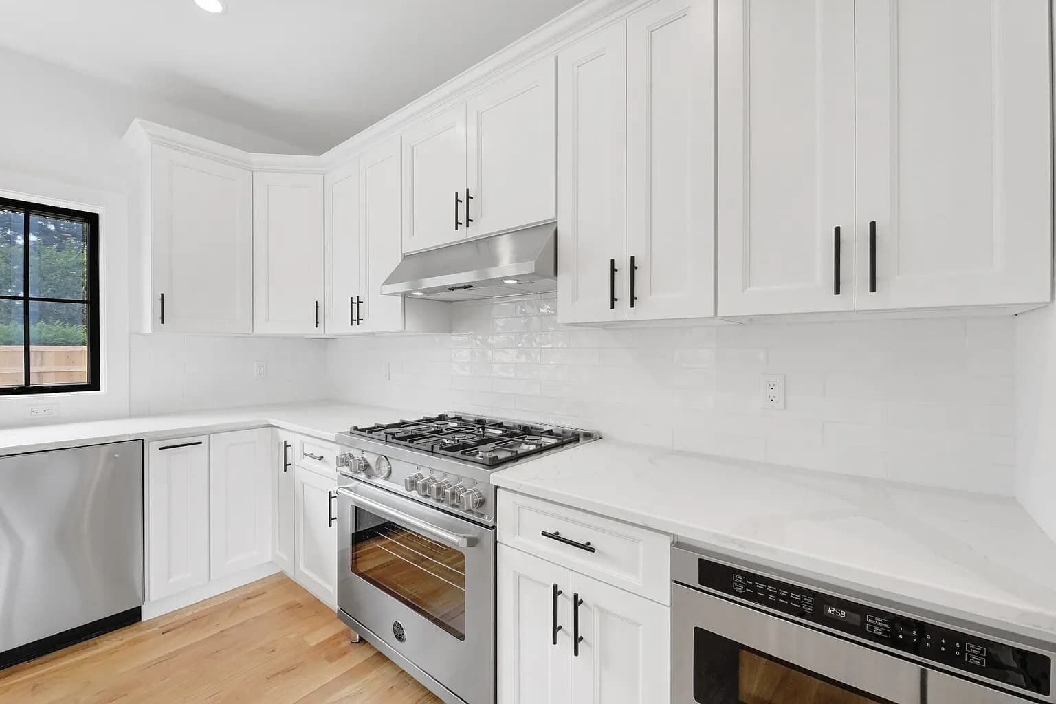 A modern kitchen with white cabinetry, stainless steel appliances, and a window providing natural light.