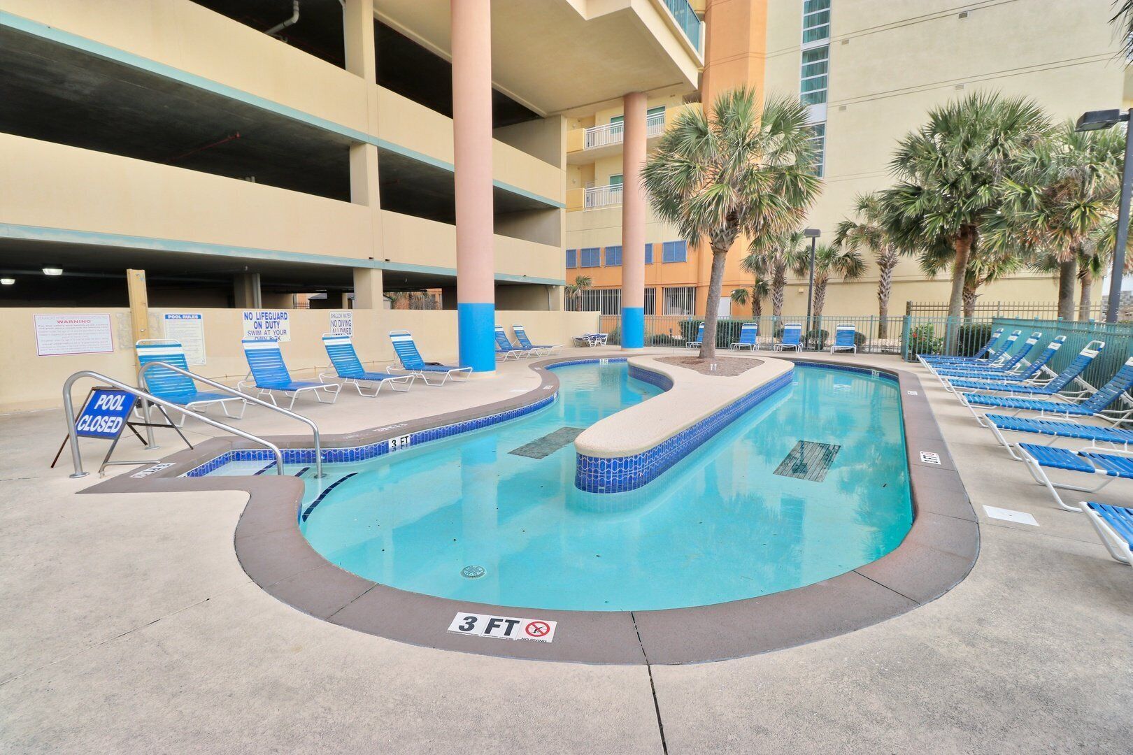 A swimming pool with blue and white tiles, surrounded by lounge chairs and palm trees.