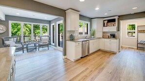 A spacious kitchen with white cabinets, a dishwasher, and a dining area with wicker chairs and a table. - Nights on Normandy (Mooresville)