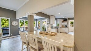 A modern kitchen with white cabinets, a central island, and a dining area with white chairs. - Nights on Normandy (Mooresville)