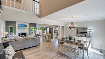 A spacious living area with a sofa, dining table, and chairs, a staircase, and a kitchen area.