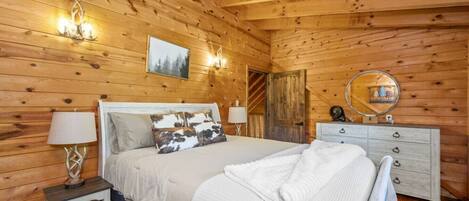 A wooden cabin bedroom with a bed, bedside lamps, a dresser, and a mirror.