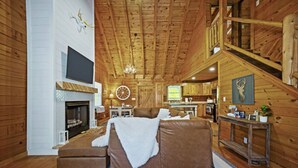 A log cabin interior with a fireplace, a large bed, a dining area, and a kitchen.