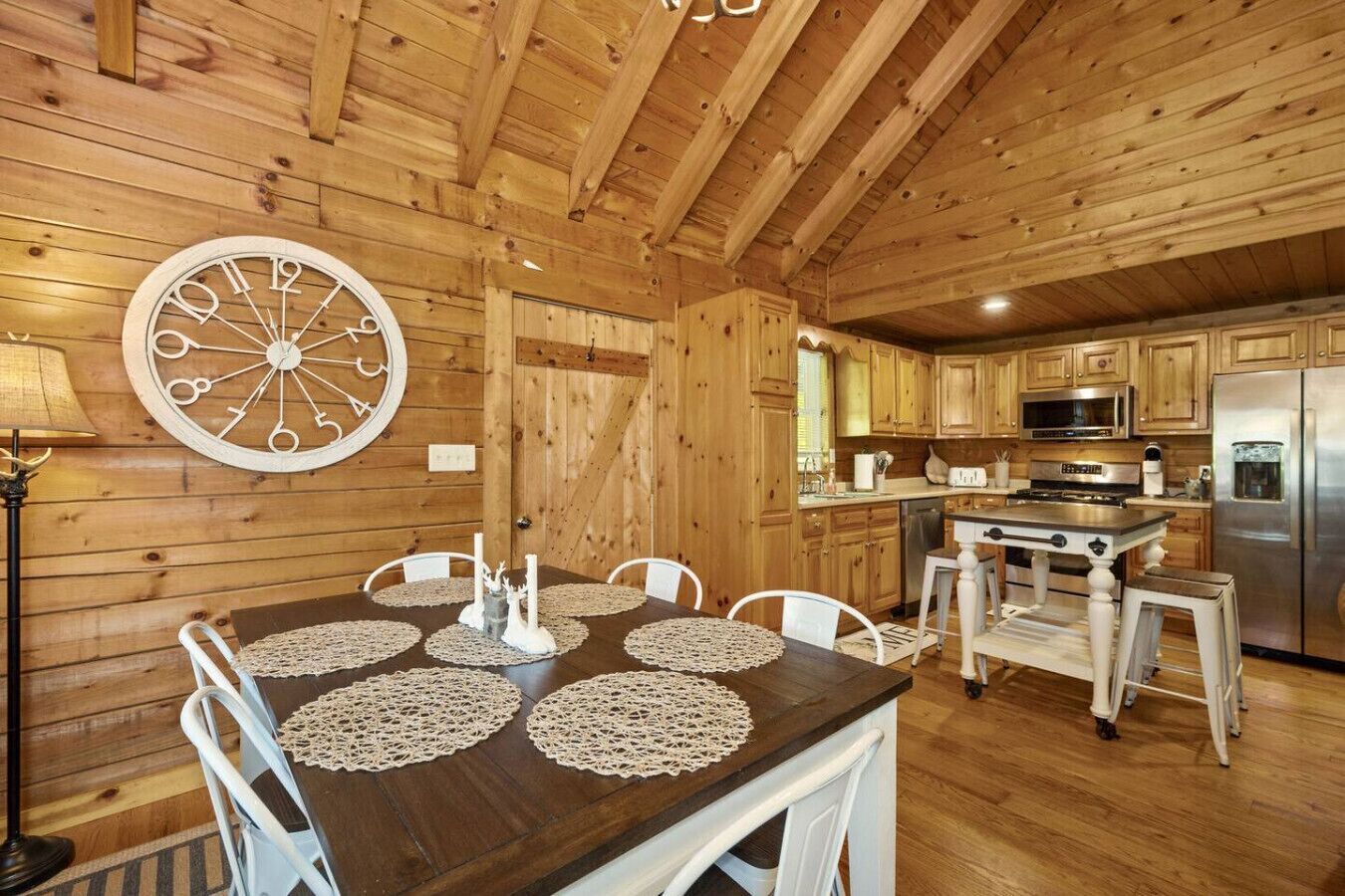 Ein Holzinterieur mit einem für vier Personen gedeckten Esstisch, einer Küchenzeile mit modernen Geräten und einer großen Wanduhr.