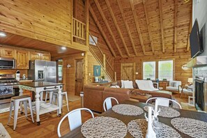 A spacious cabin with a wooden interior, a kitchen with modern appliances, a dining area with a table and chairs, and a cozy living room with a sofa and fireplace.