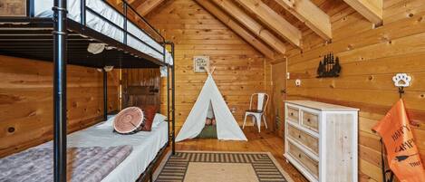 A cozy cabin with a bunk bed, a teepee, a dresser, and a sign that says "Happy Camp Tiny Bear".