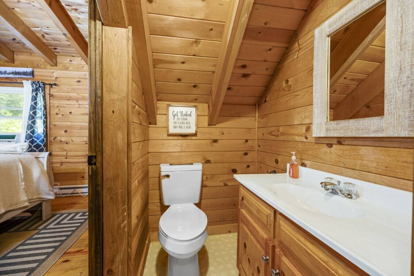 Et badeværelse i en træhytte med toilet, vask og spejl.