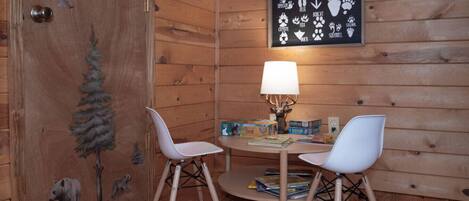 A cozy room with wooden walls, a round table with two white chairs, a lamp, and a wall sign listing animals of the woodlands.