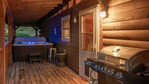 A wooden cabin with a hot tub, a barbecue grill, and a covered porch.