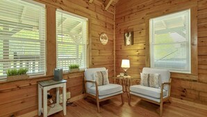 A cozy room with wooden walls, two white armchairs, a small table with a lamp, and a TV on a side table.