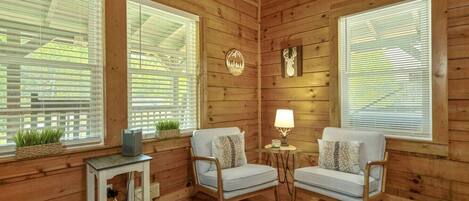 A cozy room with wooden walls, two white armchairs, a small table with a lamp, and a TV on a side table.
