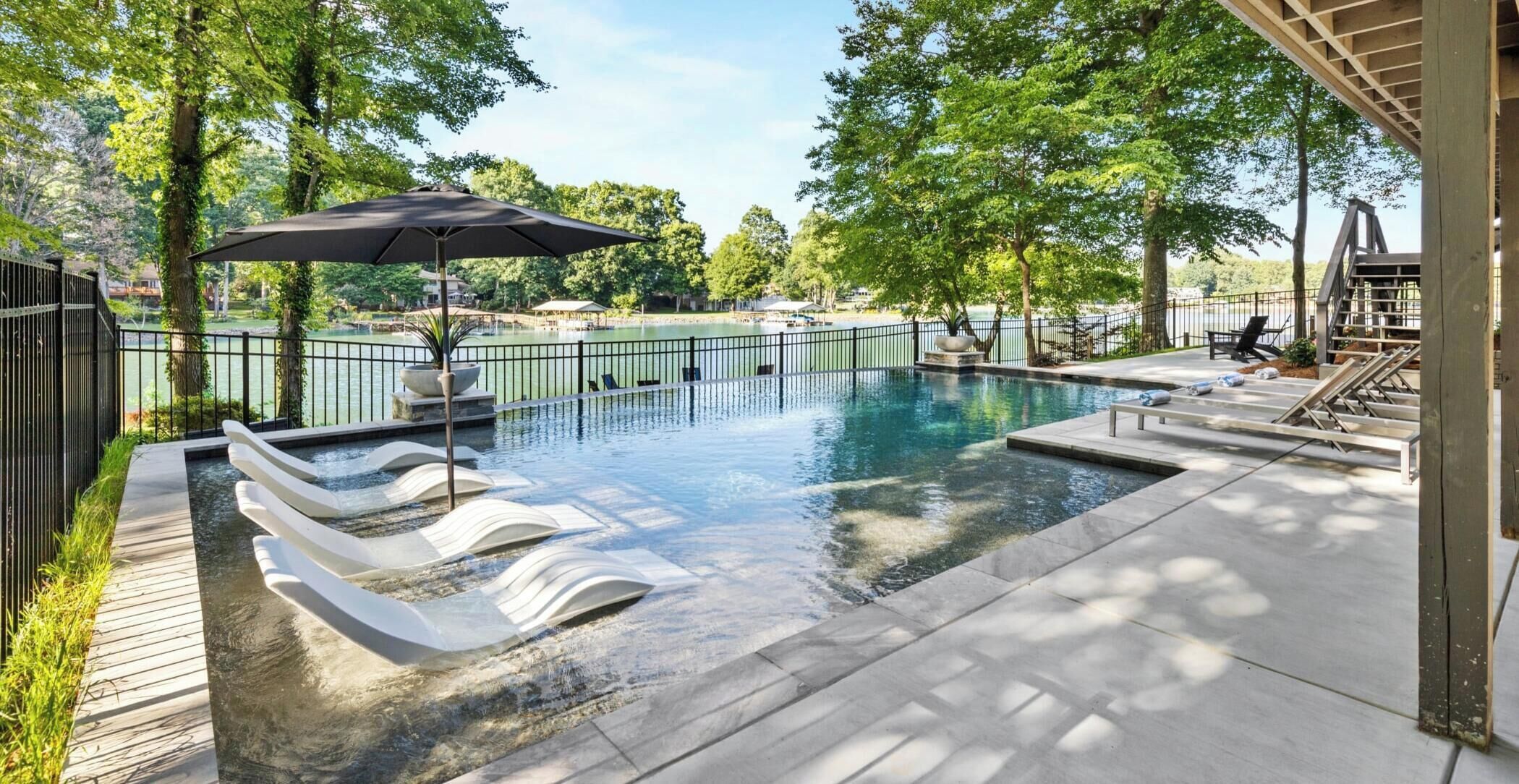 A swimming pool with a waterfall feature, surrounded by a deck and a fence.