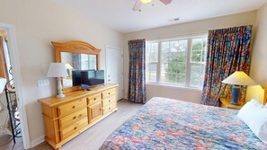 A bedroom with a bed, a dresser, a television, and a window with curtains. - Ironwood 1021 (North Myrtle Beach)