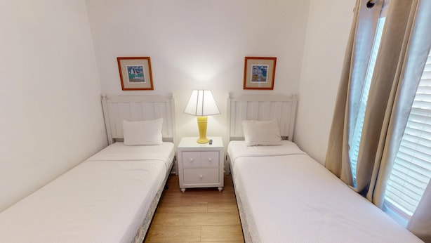 Ein Zweibettzimmer mit zwei Einzelbetten, einem Nachttisch mit Lampe und einer kleinen Schublade.