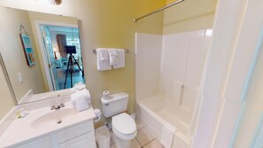 A bathroom with a bathtub, toilet, and sink. There is a mirror above the sink, and towels are hung on the wall. - Ironwood 1021 (North Myrtle Beach)