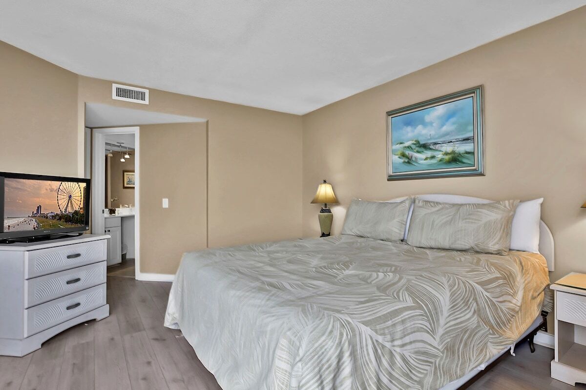 A bedroom with a bed, a television, a lamp, and a painting on the wall.
