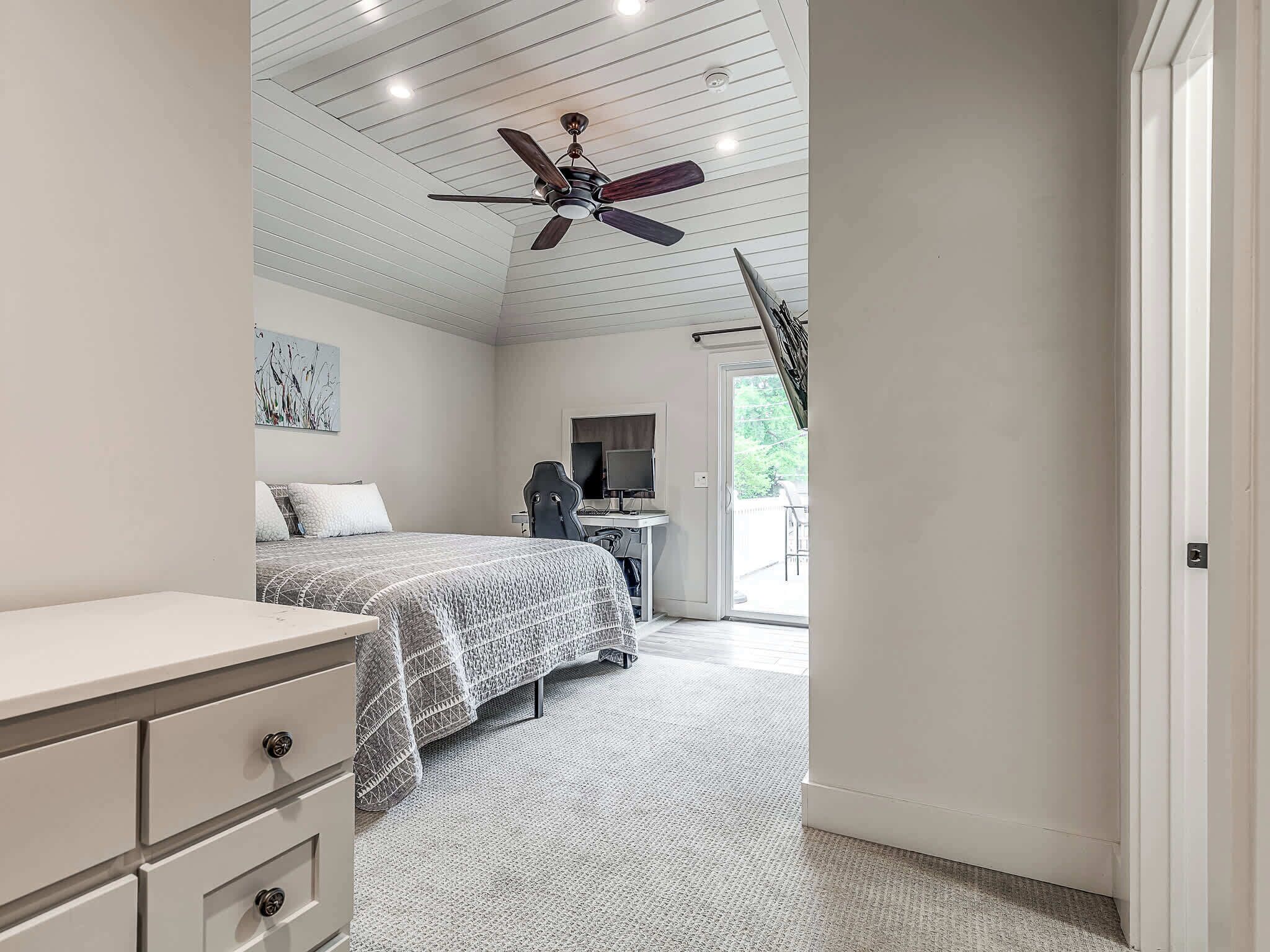 Ein Schlafzimmer mit Bett, Schreibtisch mit Computer, Deckenventilator und Blick ins Freie.