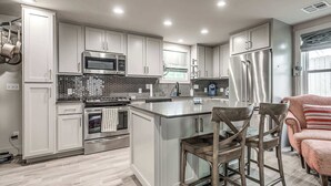 A modern kitchen with white cabinets, stainless steel appliances, and a large island with bar stools. - Cozy 1-bedroom Retreat in Tulsa (Tulsa)