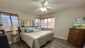 A bedroom with a bed, a dresser, a ceiling fan, and a painting on the wall. - Cape Key Updated Beach Bungalow (Ponce Inlet)