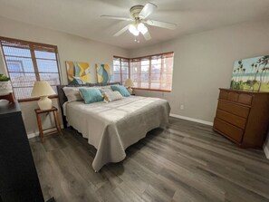 A bedroom with a bed, a dresser, a ceiling fan, and a painting on the wall. - Cape Key Updated Beach Bungalow (Ponce Inlet)