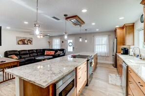 A modern kitchen with a marble island, wooden cabinets, and pendant lighting. - Cape Key Updated Beach Bungalow (Ponce Inlet)