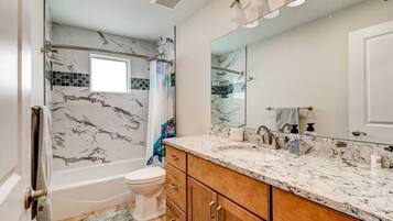 A bathroom with a shower, toilet, and vanity with a large mirror.