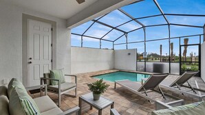 Ein überdachter Außenbereich mit Pool, Liegestühlen, einem Tisch und einer Tür.