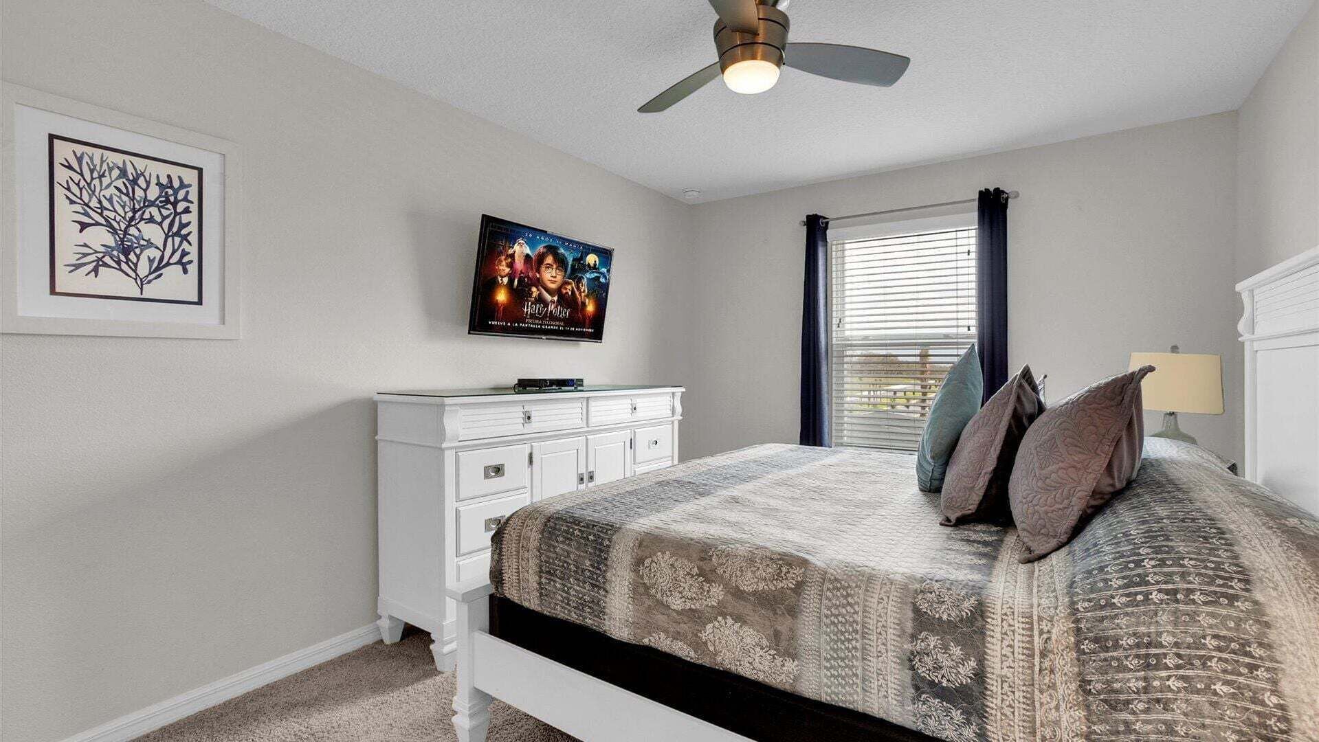 A bedroom with a bed, a dresser, a ceiling fan, a poster, and a window with curtains.