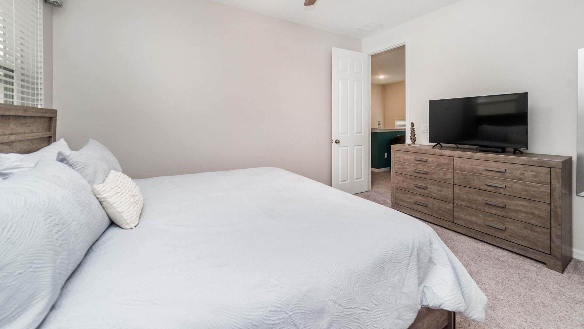 A bedroom with a bed, a dresser, a television, and a door leading to another room.
