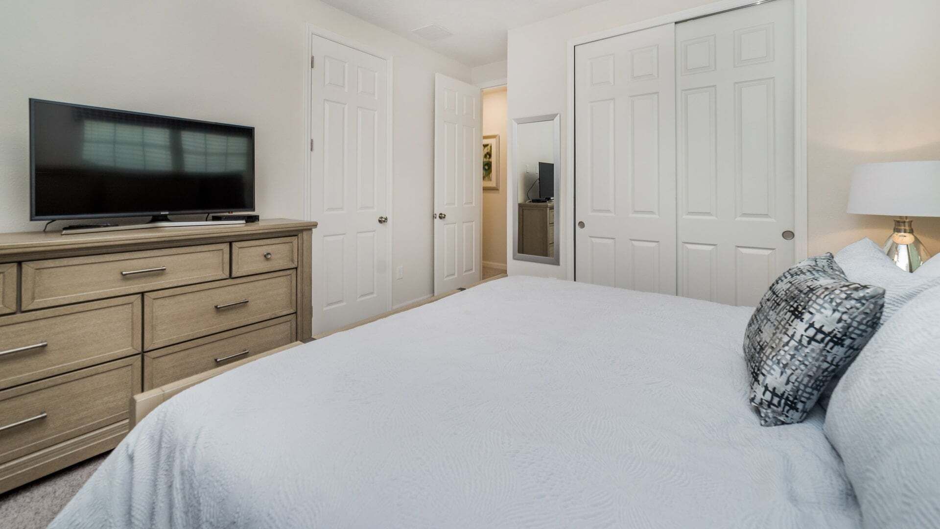 Un dormitorio con cama, cómoda, televisor y puerta que da a otra habitación.