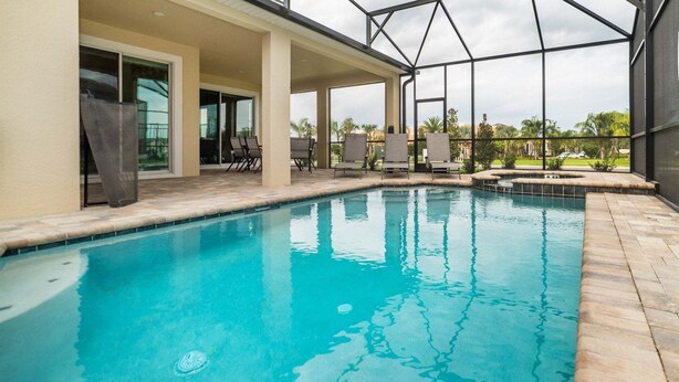 A swimming pool with a clear blue water, surrounded by a covered patio area with chairs and a glass door leading to a room. - Emt9000 (Kissimmee)