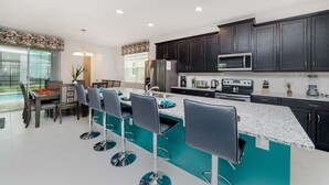 A modern kitchen with dark cabinets, a central island with bar stools, and a dining area with a view. - Emt9000 (Kissimmee)
