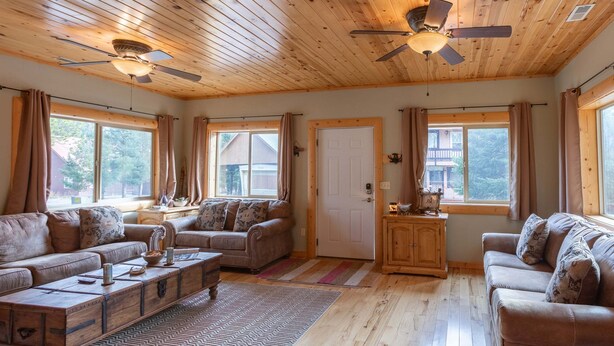 A spacious living room with wooden floors, two sofas, a coffee table, a ceiling fan, and large windows. - Muley Hollow (Island Park)