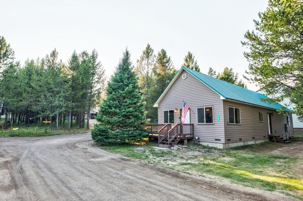 A single-story building with a green roof, a porch, and an American flag. - Muley Hollow (Island Park)