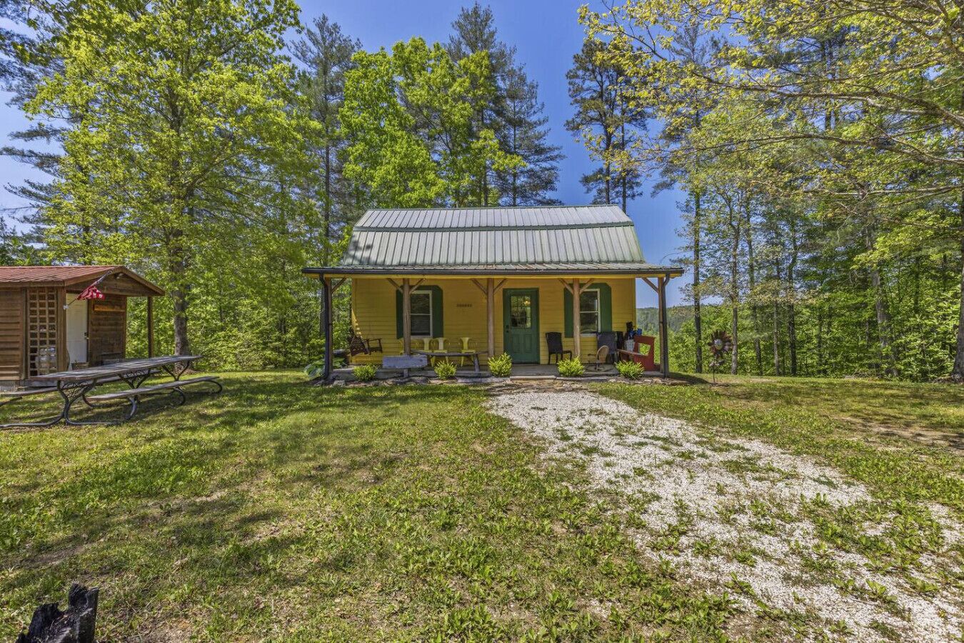 Eine gelbe Holzhütte mit Veranda, Picknicktisch und kleinem Gartenhaus.
