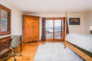 A bedroom with a wooden desk, a chair, a bed, a large wooden wardrobe, and a balcony with a view of trees and a lake. - Monthly or Seasonal Large Petite Lake 44 Lakehouse Retreat With Private Pier and Hot Tub Secluded Deep in the Woods (Antioch)