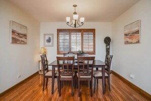 A dining room with a wooden table and chairs, a chandelier, and artwork on the walls. - Monthly or Seasonal Large Petite Lake 44 Lakehouse Retreat With Private Pier and Hot Tub Secluded Deep in the Woods (Antioch)