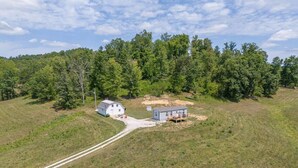 A rural property with a large white barn, a small blue house, and a dirt path leading to the barn. - Wifi, Firepit, Fishing Pond - Farmview (Hazel Green)