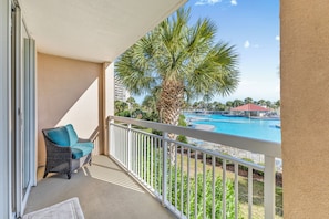 A balcony with a wicker chair and a view of a swimming pool and palm trees. - North Tower 208 (North Myrtle Beach)